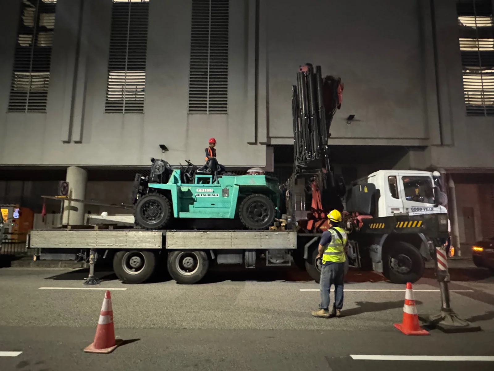 Heavy forklift transported on lorry crane truck at night
